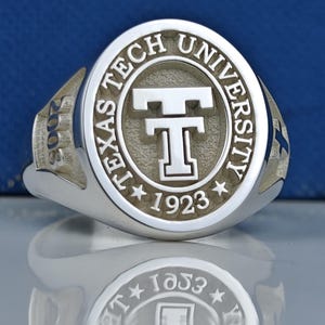 May include: A silver ring with a raised oval design featuring the words "Texas Tech University" and a large "T" in the center. The year "1923" is inscribed below the "T" and the year "2008" is inscribed on the side of the ring.