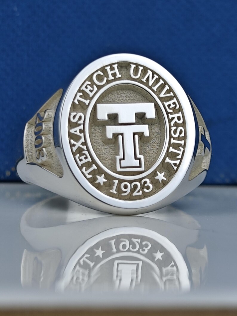 May include: A silver ring with a raised oval design featuring the words "Texas Tech University" and a large "T" in the center. The year "1923" is inscribed below the "T" and the year "2008" is inscribed on the side of the ring.