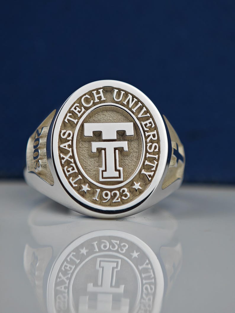 May include: A silver ring with a gold-toned center featuring the Texas Tech University logo and the year 1923.