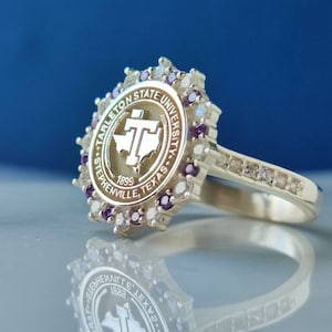 May include: A silver ring with a purple and white stone setting. The ring features the Tarleton State University logo, which includes the words "Tarleton State University", "Stephenville, Texas", and "1899".