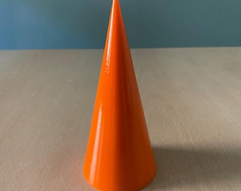 Könnte beinhalten: Eine leuchtend orangefarbene, kegelförmige Kerze mit einem weißen Docht. Die Kerze hat eine glatte, glänzende Oberfläche und steht auf einer Holzoberfläche. Der Hintergrund ist einfarbig hellblau.