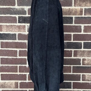 May include: A black bomber jacket with a ribbed collar and cuffs. The jacket is made of a soft, textured material and has a relaxed fit. The jacket is hanging against a brick wall.
