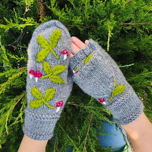 以下が含まれることがあります： 緑の葉と白い斑点のある小さな赤いキノコが刺繍された、グレーのニットミトン。リブ編みの袖口と、指先を出したり覆ったりできるコンバーチブルフラップデザインが特徴の、手袋のペア。