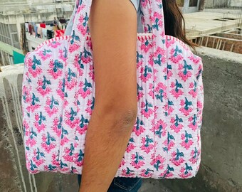 May include: A white tote bag with a pink and blue floral print. The bag has two handles and is made of quilted fabric.