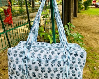 May include: A white and blue floral print tote bag with matching handles. The bag features a rectangular shape with a pocket on the front. The floral pattern is repeated across the bag's surface.