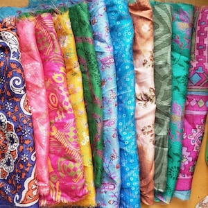 May include: A collection of colourful silk fabric scraps with various patterns, including floral, paisley, and geometric designs. The fabrics are arranged in a row, showcasing their vibrant hues and intricate details.