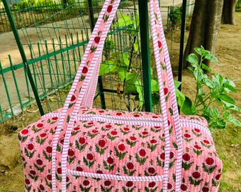 May include: A pink and white floral print duffel bag with a zipper closure and two top handles. The bag is made of quilted fabric and has a small pocket on the front.