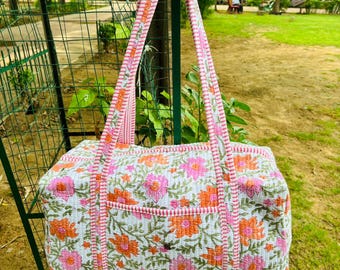 May include: A pink and white floral print duffel bag with a pink and white striped strap. The bag has a small pocket on the front.