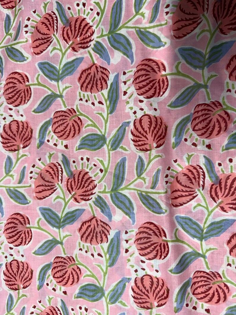 Pu&ograve; includere: Tessuto rosa con un motivo floreale ripetuto. Il design presenta grandi fiori stilizzati nei toni del rosso e del rosa, con steli verdi e foglie blu. Lo sfondo &egrave; rosa tenue.