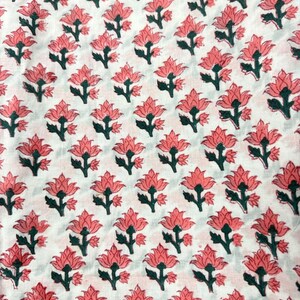 May include: White fabric with a repeating pattern of pink flowers and green stems. The flowers are stylized with multiple petals, and the pattern is evenly spaced across the fabric.