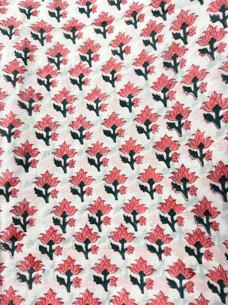 May include: White fabric with a repeating pattern of pink flowers and green stems. The flowers are stylized with multiple petals, and the pattern is evenly spaced across the fabric.