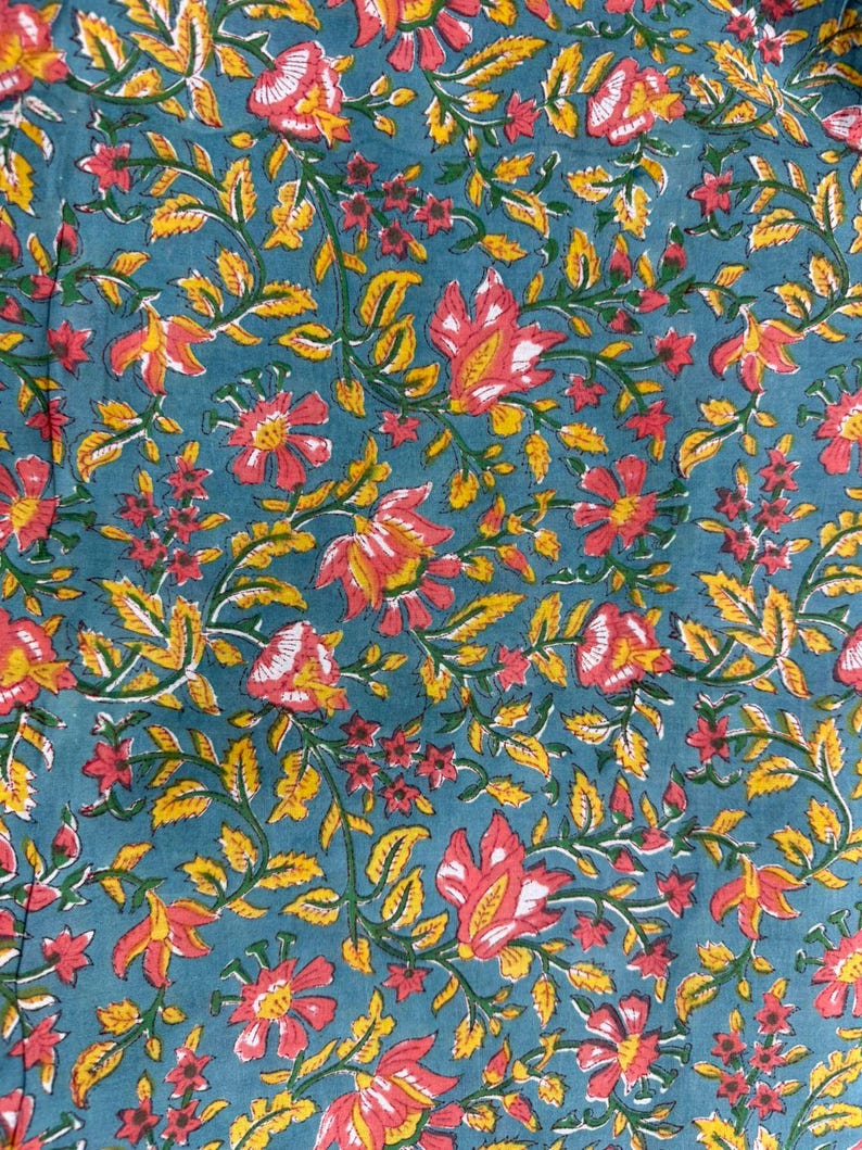 May include: Close-up of a teal fabric with a floral pattern. The design features red and yellow flowers with green leaves and vines. The flowers have white accents, and the leaves are a bright yellow.