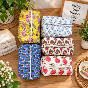 May include: Five rectangular quilted cosmetic bags with white zippers, featuring various floral block-print patterns in yellow, blue, white, and pink. The bags are arranged in a group, showcasing distinct color palettes and botanical designs on each piece.
