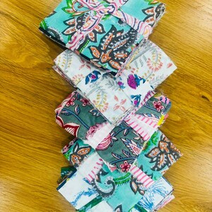 May include: A stack of colorful fabric squares with floral patterns in shades of teal, pink, white, and gray. The fabric is folded and stacked, showcasing the variety of designs and colors.