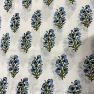 Pu&ograve; includere: Tessuto bianco con un motivo ripetuto di bouquet floreali blu con steli e foglie verdi. I fiori hanno un aspetto dettagliato e stratificato. Il tessuto &egrave; probabilmente in cotone o lino, adatto per abbigliamento o arredamento.