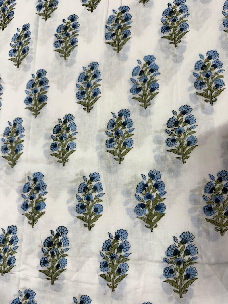 Pu&ograve; includere: Tessuto bianco con un motivo ripetuto di bouquet floreali blu con steli e foglie verdi. I fiori hanno un aspetto dettagliato e stratificato. Il tessuto &egrave; probabilmente in cotone o lino, adatto per abbigliamento o arredamento.
