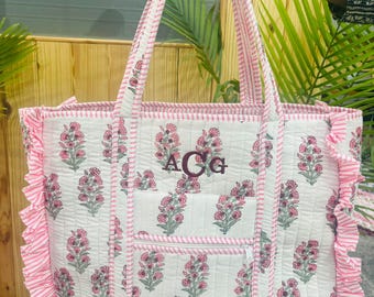 May include: Quilted white tote bag with a pink floral design and frill trim. Includes a front pocket and striped pink and white handles. The bag has the initials "ACG" embroidered on the front.