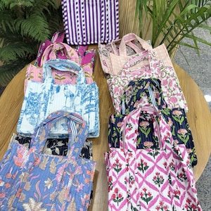 Könnte beinhalten: Eine Sammlung kleiner Tragetaschen mit verschiedenen floralen und geometrischen Mustern. Die Taschen bestehen aus gestepptem Stoff in Blau-, Rosa- und Lilatönen. Einige Taschen haben Streifen- oder Karomuster. Jede Tasche hat einen passenden Griff.