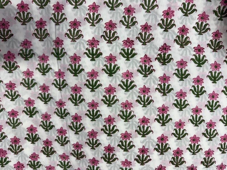 Puede incluir: Una tela blanca con un patr&oacute;n de estampado de bloques repetitivo de peque&ntilde;as flores rosas con tallos y hojas verdes. Los motivos florales est&aacute;n dispuestos en una formaci&oacute;n de cuadr&iacute;cula sobre la superficie, creando un dise&ntilde;o bot&aacute;nico sim&eacute;trico.