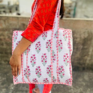 Op de afbeelding: Een witte katoenen tote bag met roze bloemenprint en roze en witte gestreepte afwerking. De tas heeft twee lange hengsels.
