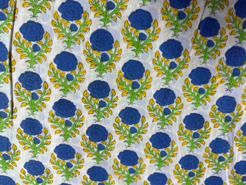 Pu&ograve; includere: Tessuto bianco con un motivo ripetuto di fiori blu, steli verdi e foglie gialle. Il design &egrave; uniformemente distanziato, creando una disposizione simmetrica. Il tessuto sembra essere di cotone, adatto a vari progetti tessili.