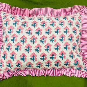 May include: A rectangular pillow featuring a white base with a repeating pattern of pink flowers and blue stems. The pillow is bordered by a wide, gathered ruffle trim in a pink and white vertical stripe pattern, creating a decorative edge.