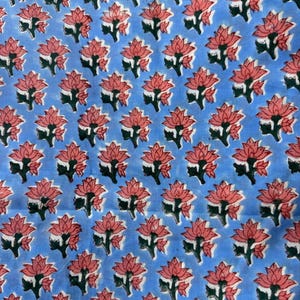 Pu&ograve; includere: Un tessuto azzurro con un motivo ripetuto di fiori di loto rosa e foglie verdi. Il motivo floreale &egrave; uniformemente distribuito sul tessuto, creando una disposizione simmetrica. Il tessuto sembra essere di cotone o un materiale simile.