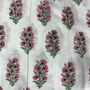 Puede incluir: Una tela blanca con un patr&oacute;n repetitivo de motivos florales. Cada motivo consiste en un grupo de flores rosas con tallos y hojas verdes. La superficie de la tela muestra sutiles l&iacute;neas verticales a lo largo de todo el material.
