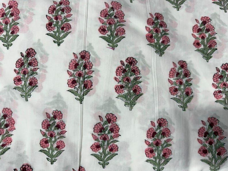 Puede incluir: Una tela blanca con un patr&oacute;n repetitivo de motivos florales. Cada motivo consiste en un grupo de flores rosas con tallos y hojas verdes. La superficie de la tela muestra sutiles l&iacute;neas verticales a lo largo de todo el material.