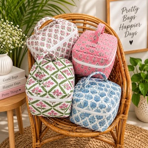 May include: Four quilted fabric cosmetic bags with top handles and white zippers. One bag is white with pink floral patterns, one is solid pink with floral prints, one features a green lattice design with pink flowers, and one has blue floral patterns.