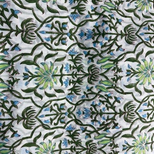 May include: White fabric with a repeating floral pattern in green, light green, and blue. The design features stylized flowers, leaves, and bird-like shapes, creating a botanical theme. The fabric has a soft, slightly wrinkled appearance.