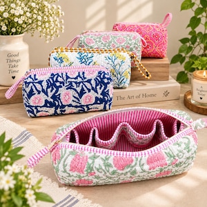 May include: A collection of rectangular quilted fabric pouches featuring various floral block print patterns in pink, blue, green, and yellow. Each pouch includes a zipper closure with a striped fabric pull tab and a pink and white striped interior lining.