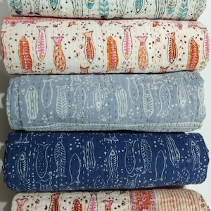 Peut inclure: Cinq rouleaux de tissu avec un fond blanc et un motif répétitif de poissons bleus, orange et gris. Le tissu est plié et empilé les uns sur les autres.