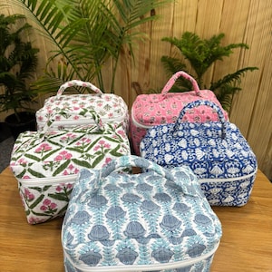 Può includere: Cinque trousse per cosmetici con motivi floreali e botanici. Le borse presentano disegni in rosa, blu e verde su sfondi bianchi. Ogni borsa ha un manico superiore e una chiusura a zip. Sono appoggiate su una superficie di legno.