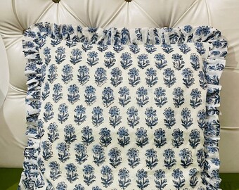 May include: A square throw pillow featuring a repeating blue floral pattern on a white background. The pillow is finished with a gathered fabric ruffle trim along all four edges, creating a decorative border that frames the central floral design.