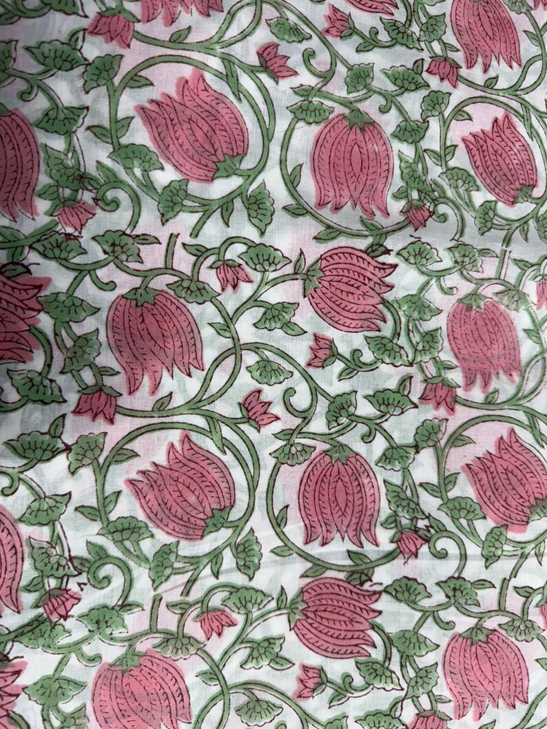 Puede incluir: Una tela blanca con un patr&oacute;n de estampado en bloque repetitivo de flores rosadas similares a lotos con tallos y hojas verdes. El dise&ntilde;o consiste en enredaderas interconectadas y motivos florales distribuidos uniformemente por la superficie.