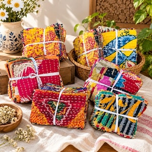 May include: Several stacks of folded fabric squares featuring vibrant, multi-colored patterns and intricate white running stitch details. Each bundle is secured with a white string, showcasing various floral and geometric prints in shades of yellow, pink, blue, and orange.