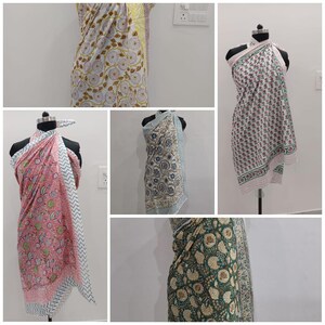 May include: Collection of colorful sarongs with floral patterns. The sarongs are displayed on mannequins, showcasing various designs. The colors include white, pink, green, blue, and yellow, with intricate floral and geometric prints. The sarongs are made of lightweight fabric.