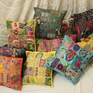 Può includere: Una collezione di cuscini patchwork colorati con ricami intricati e dettagli perlati. I cuscini sono disposti su una superficie bianca e presentano una varietà di motivi e colori, tra cui giallo, blu, verde, rosso e arancione.