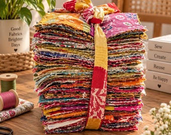 May include: A tall stack of square fabric scraps featuring a variety of colorful floral and geometric patterns in shades of yellow, pink, red, and blue. The stack is tied together with a long strip of matching patterned fabric knotted at the top.