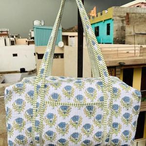 May include: A white cotton duffel bag with a blue and green floral print. The bag has two long straps and a zip closure.