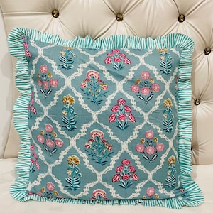 May include: A square throw pillow featuring a teal blue background with a white lattice pattern and repeating floral motifs in pink and yellow. The pillow is finished with a ruffled border in a teal and white striped fabric along all four edges.
