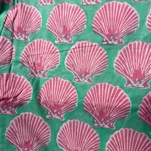 Pu&ograve; includere: Un motivo ripetuto di conchiglie rosa con strisce bianche su uno sfondo verde acqua. Le conchiglie sono uniformemente distanziate e creano un design estivo a tema spiaggia. L'immagine &egrave; un primo piano del tessuto.