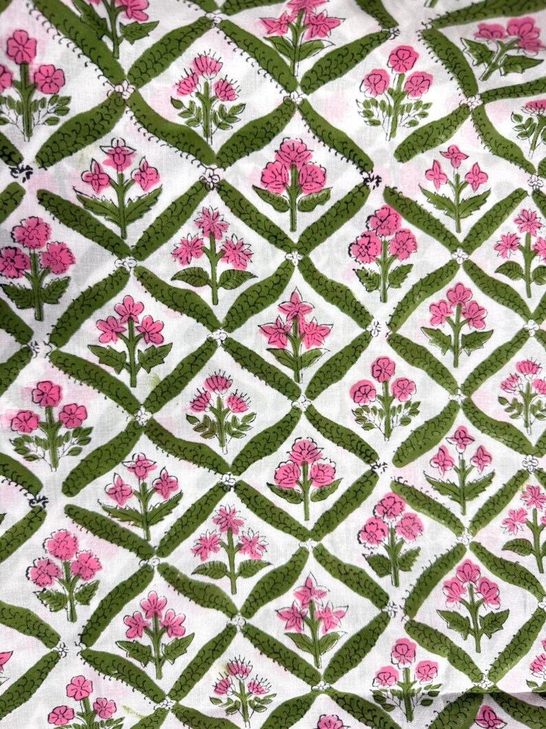 Puede incluir: Una tela blanca con un patr&oacute;n repetitivo de diamantes delineados en verde oliva. Cada diamante contiene una ilustraci&oacute;n centrada de una flor rosa con hojas y tallos verdes. El dise&ntilde;o es sim&eacute;trico y cubre toda la superficie visible.