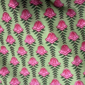 May include: Close-up of a fabric with a repeating floral pattern. The design features pink bell-shaped flowers with green leaves and stems against a light green background. The pattern is symmetrical and detailed.