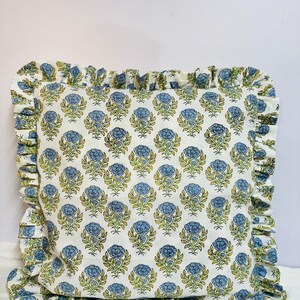 May include: A square throw pillow featuring a repeating floral pattern of blue blossoms and green leaves on a white background. The pillow is finished with a gathered fabric ruffle trim along all four edges, matching the floral print of the cover.