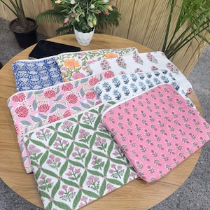 May include: A collection of colorful, floral-patterned pouches. The pouches feature various designs, including pink roses, blue floral patterns, and orange blooms. The pouches are arranged on a wooden table, showcasing their vibrant colors and intricate designs.