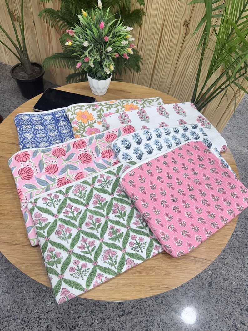 May include: A collection of colorful, floral-patterned pouches. The pouches feature various designs, including pink roses, blue floral patterns, and orange blooms. The pouches are arranged on a wooden table, showcasing their vibrant colors and intricate designs.