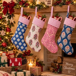 Puede incluir: Cuatro calcetines navideños de tela colgados en fila, cada uno con un puño de rayas rosas y blancas. Los calcetines muestran varios patrones florales y ornamentados en tonos azul, blanco y rosa, con pequeñas cajas de regalo en su interior.