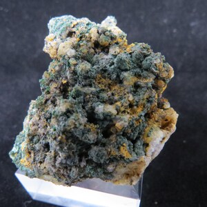 Puede incluir: Un cúmulo de minerales verdes y amarillos sobre una roca blanca. Los minerales están dispuestos en un patrón irregular y áspero.